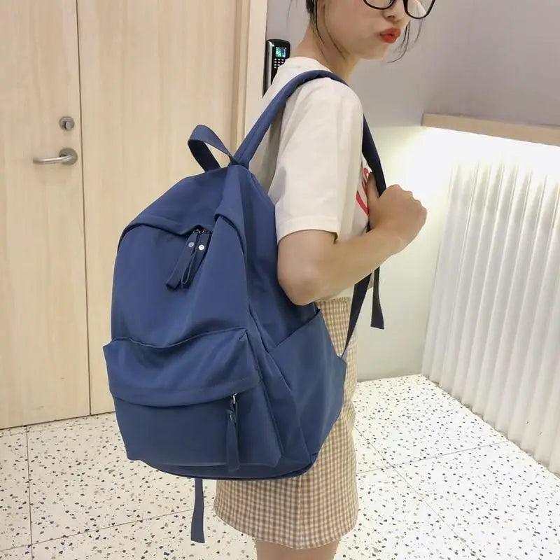 Dark blue backpack with front zip pocket and dangling zipper pulls, worn