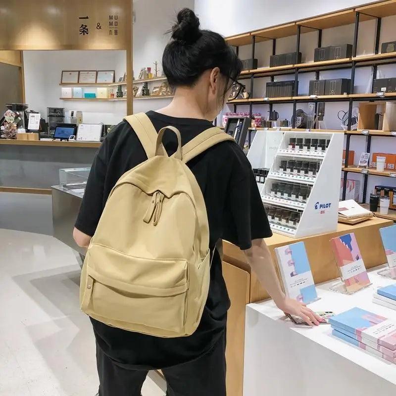 Beige backpack with adjustable straps and small front pocket, back view