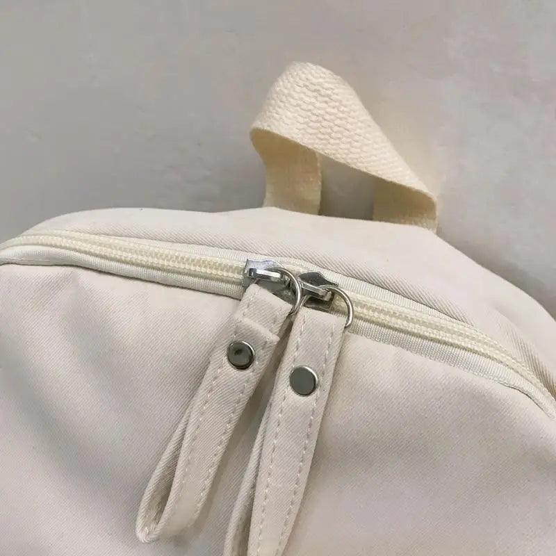 Cream backpack with top zipper and metal pull rings