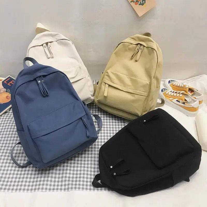 Solid-color backpacks in blue, tan, white, and black with front pockets and zips
