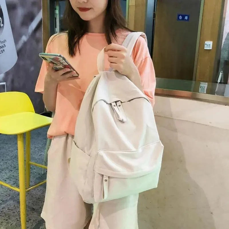 Light cream backpack with front pocket and top handle, worn outdoors