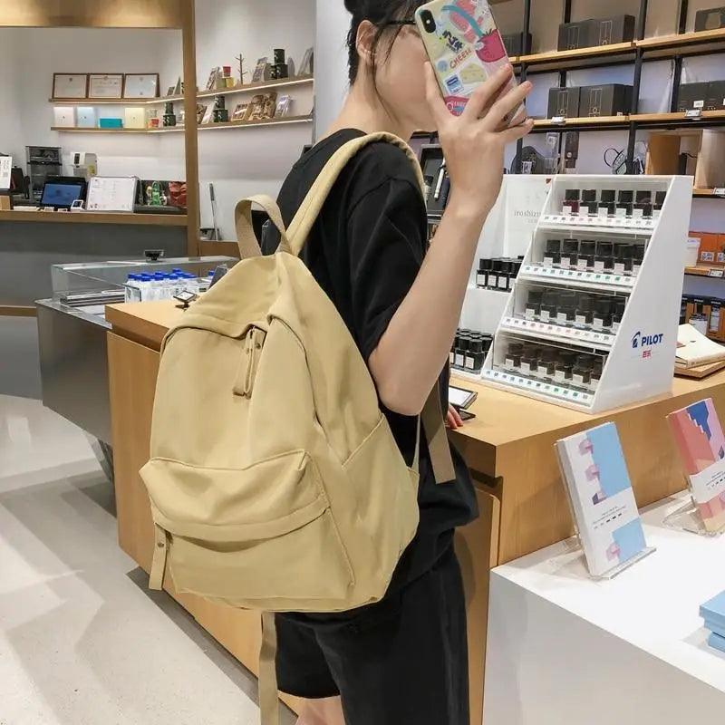 Beige mini backpack with front pocket, drawstring cords, and adjustable shoulder straps