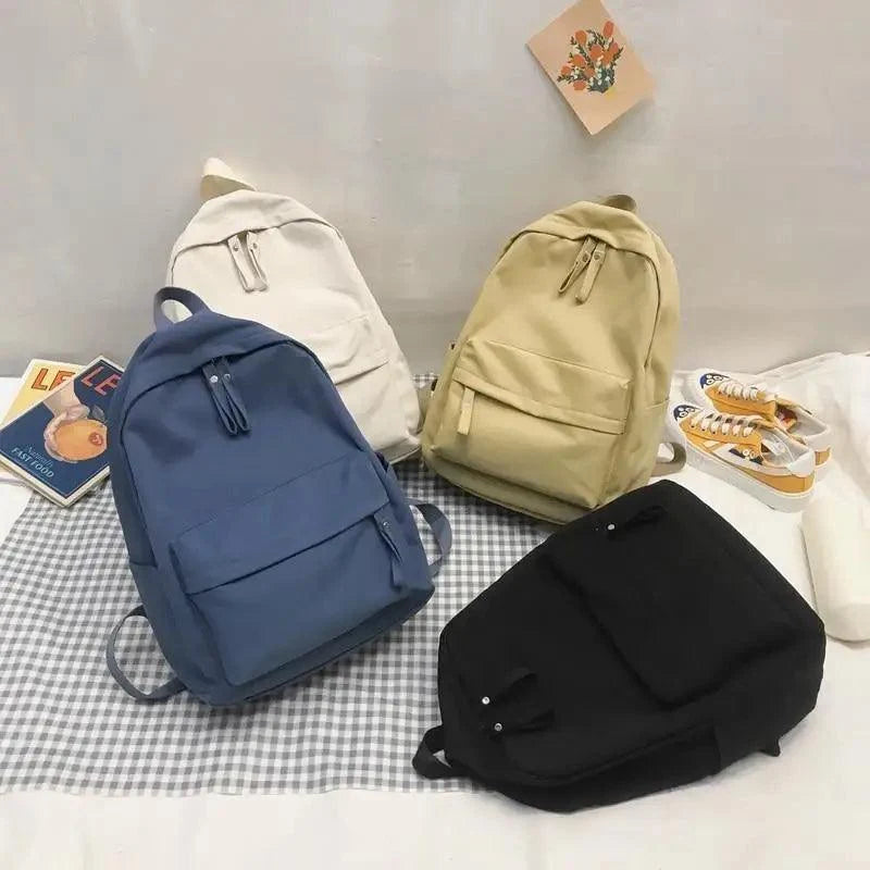 Assorted backpacks in navy, black, cream, and khaki, each with front pocket