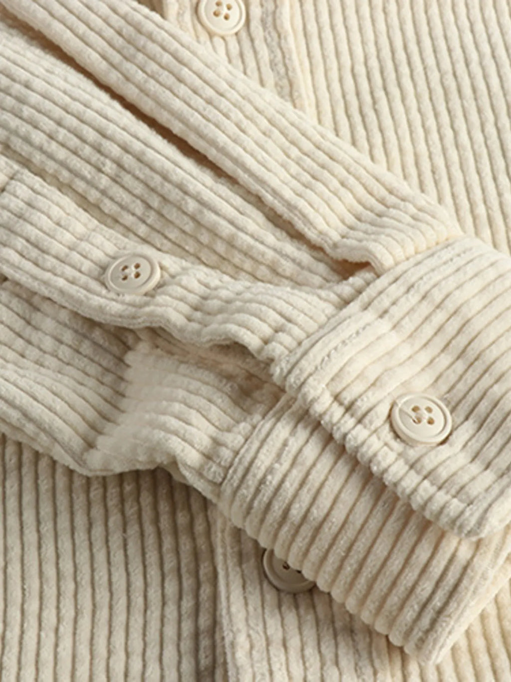 Close-up of light beige corduroy button placket with round buttons and ribbed texture