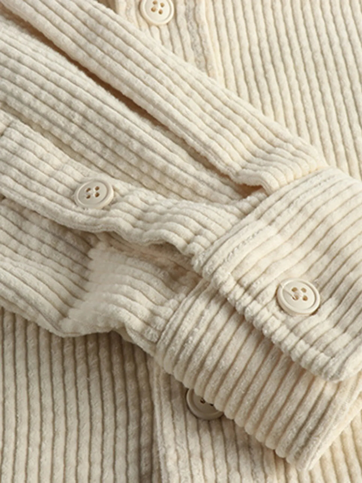 Close-up of light beige corduroy button placket with round buttons and ribbed texture