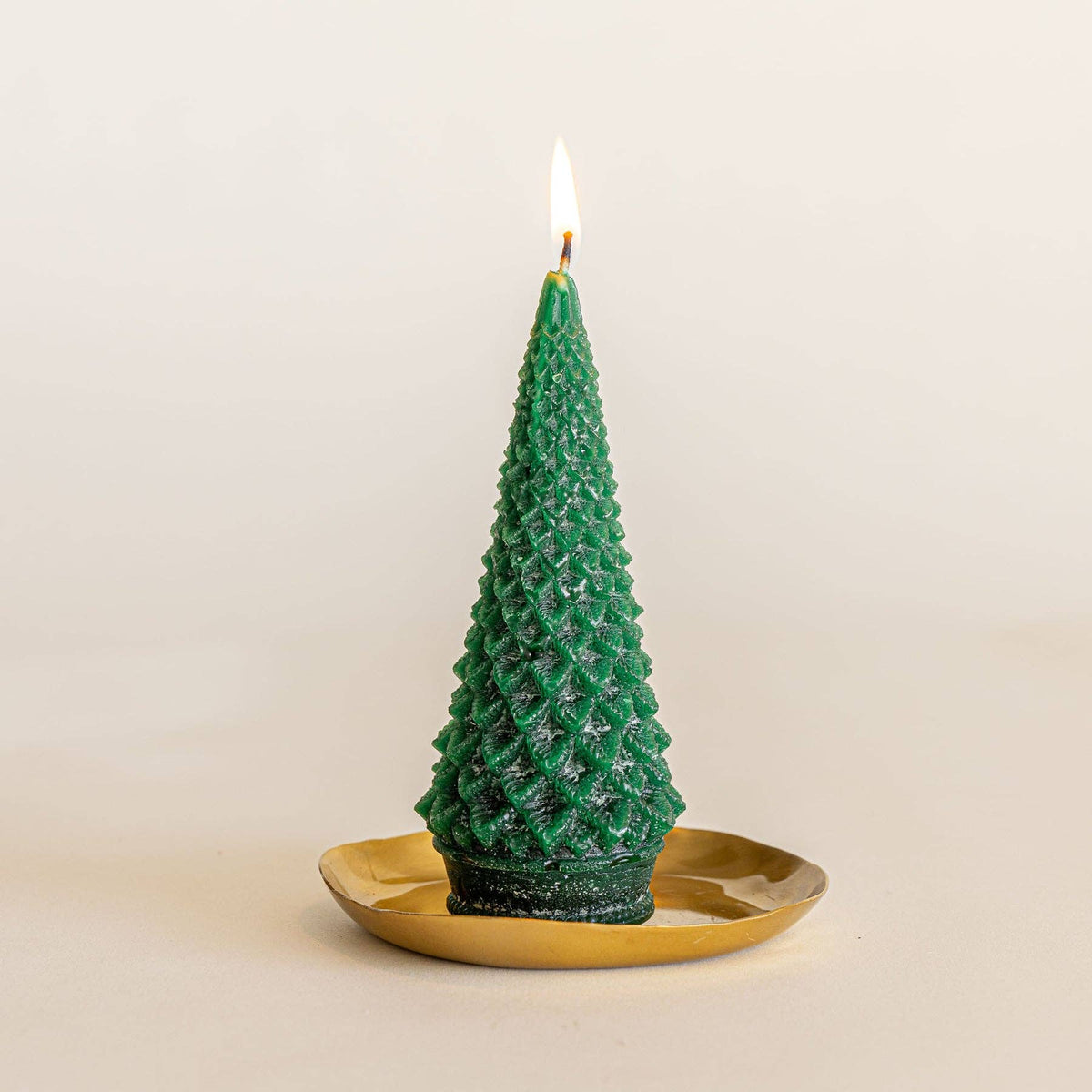 Green sculpted tree-shaped candle on round gold plate, flame lit