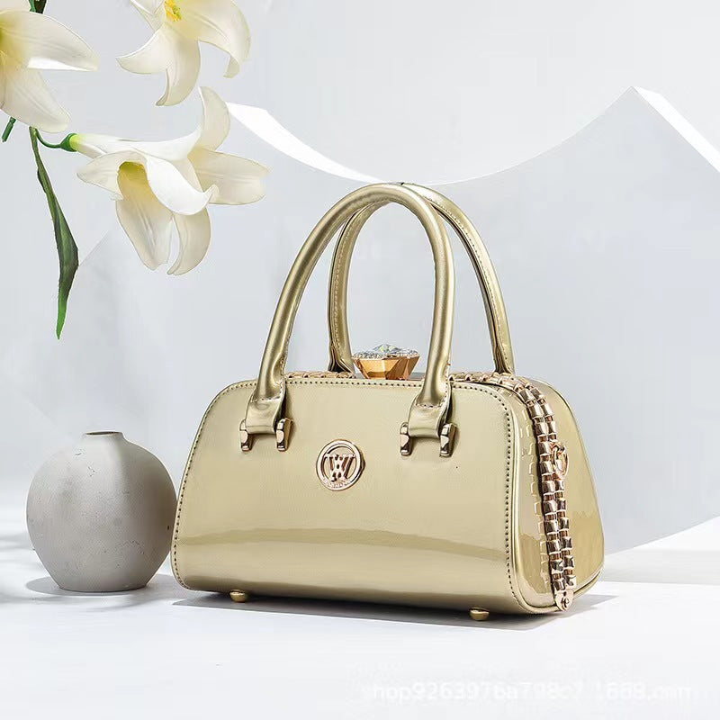 Gold patent leather handbag with top handles, chain strap, and diamond clasp
