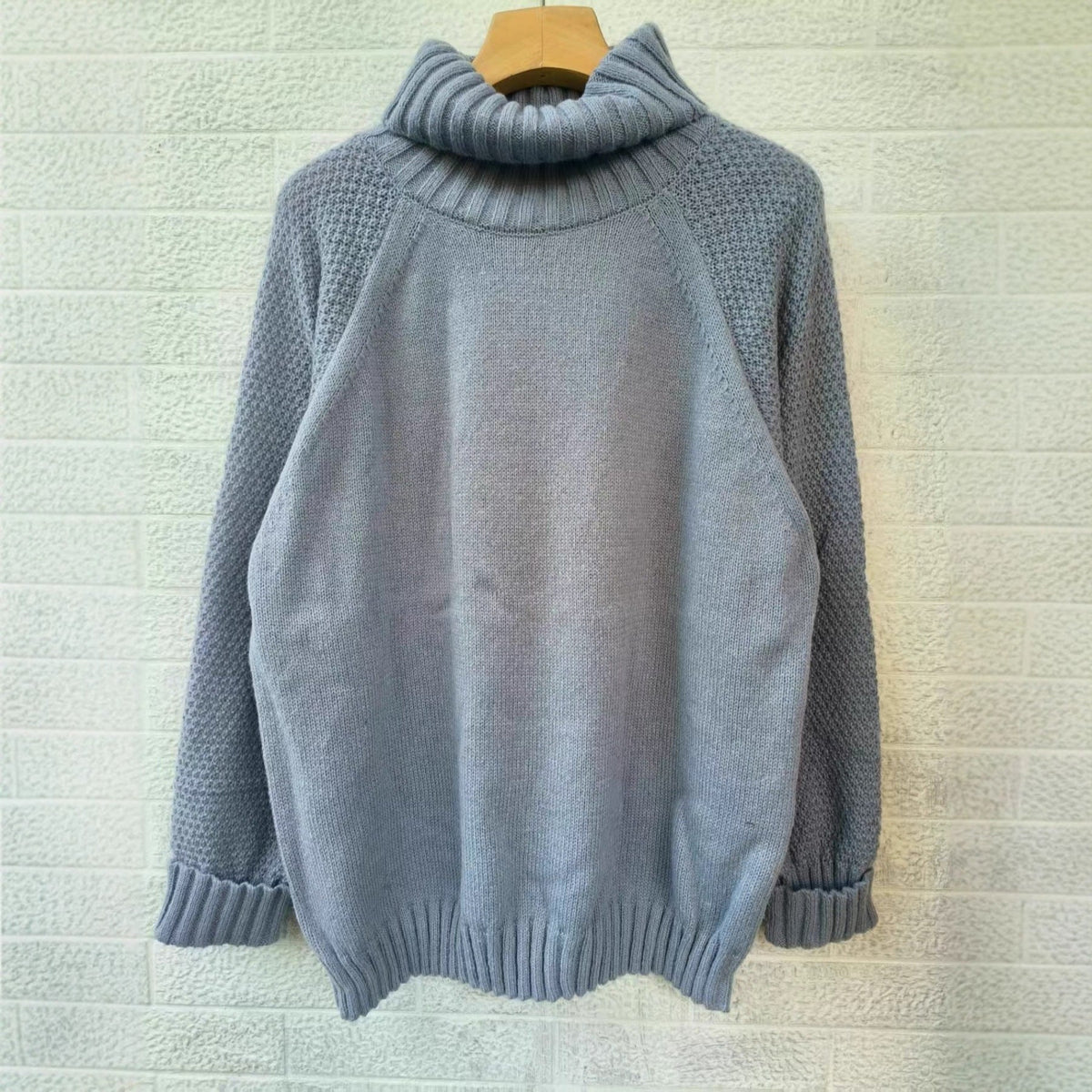 Gray knitted turtleneck sweater on hanger with long sleeves and ribbed bottom