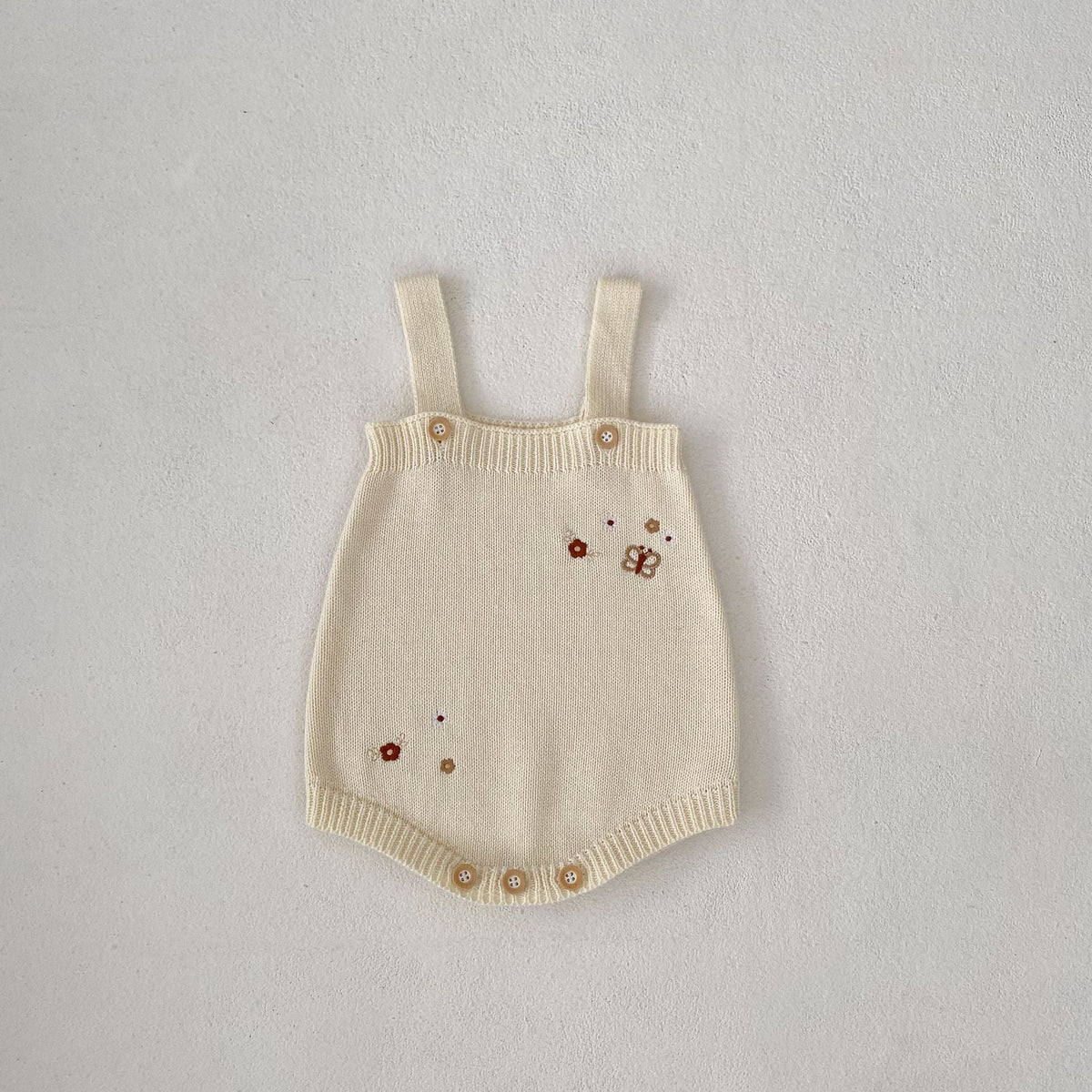 Infant cream knit romper with contrast straps and small embroidered motifs
