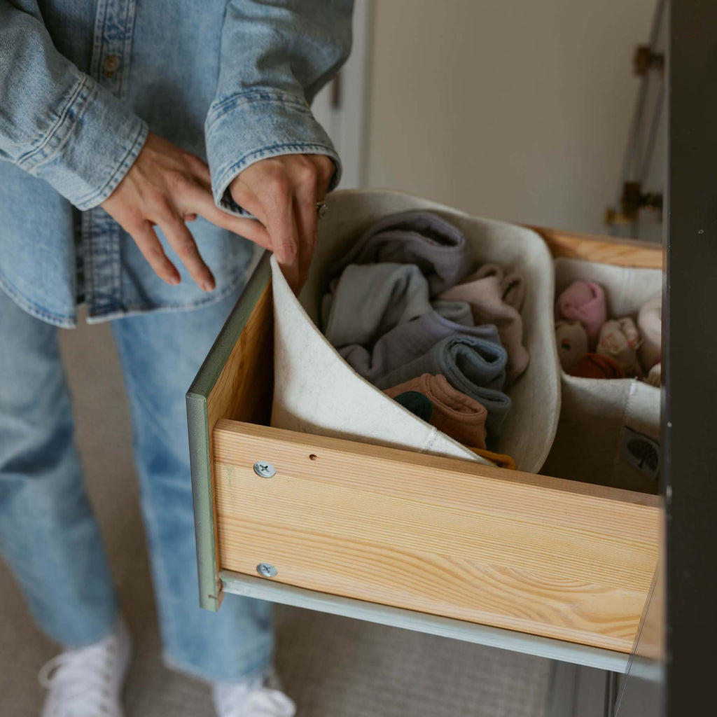 Wood-framed drawer insert with white felt organizers holding folded baby clothes