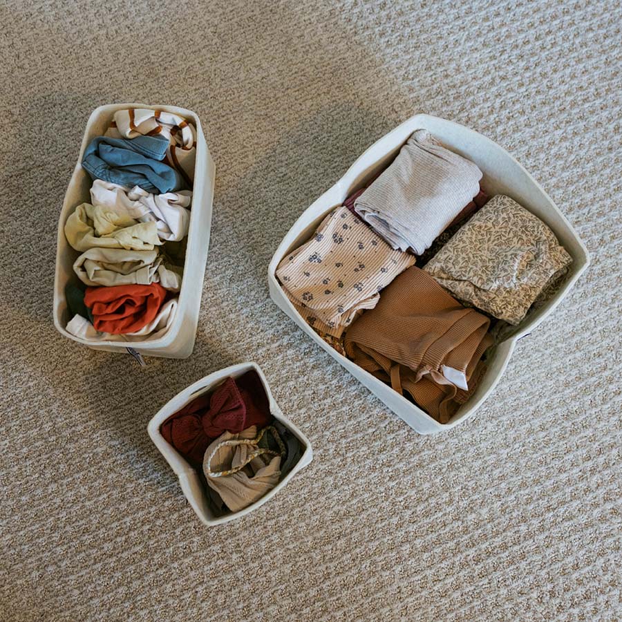 Three white felt drawer organizer bins on carpet, filled with folded clothes
