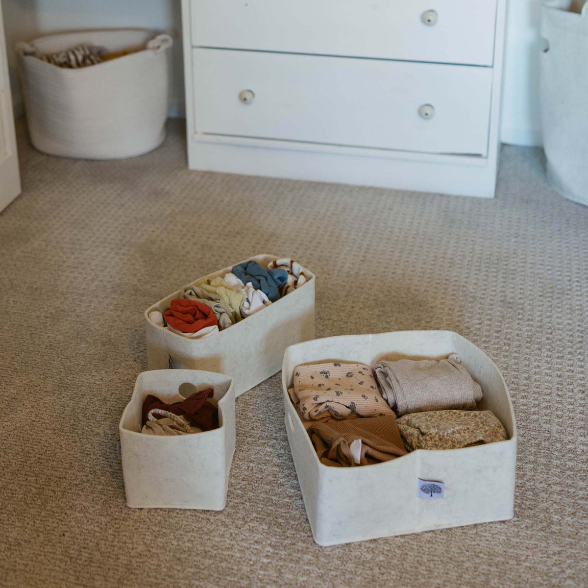 Three white felt drawer organizer bins on carpet, each with folded baby clothing