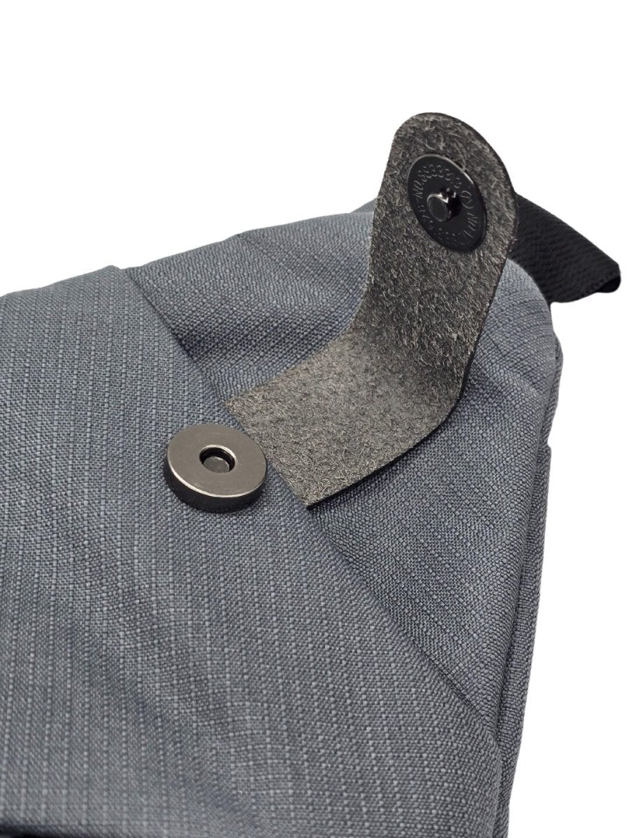 Gray crossbody bag corner with felt-lined collar tab and round metal snap.