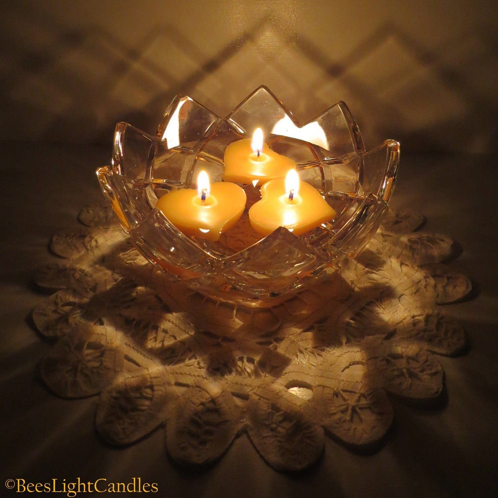 Floating heart-shaped candles in a clear glass bowl, three lit wicks visible