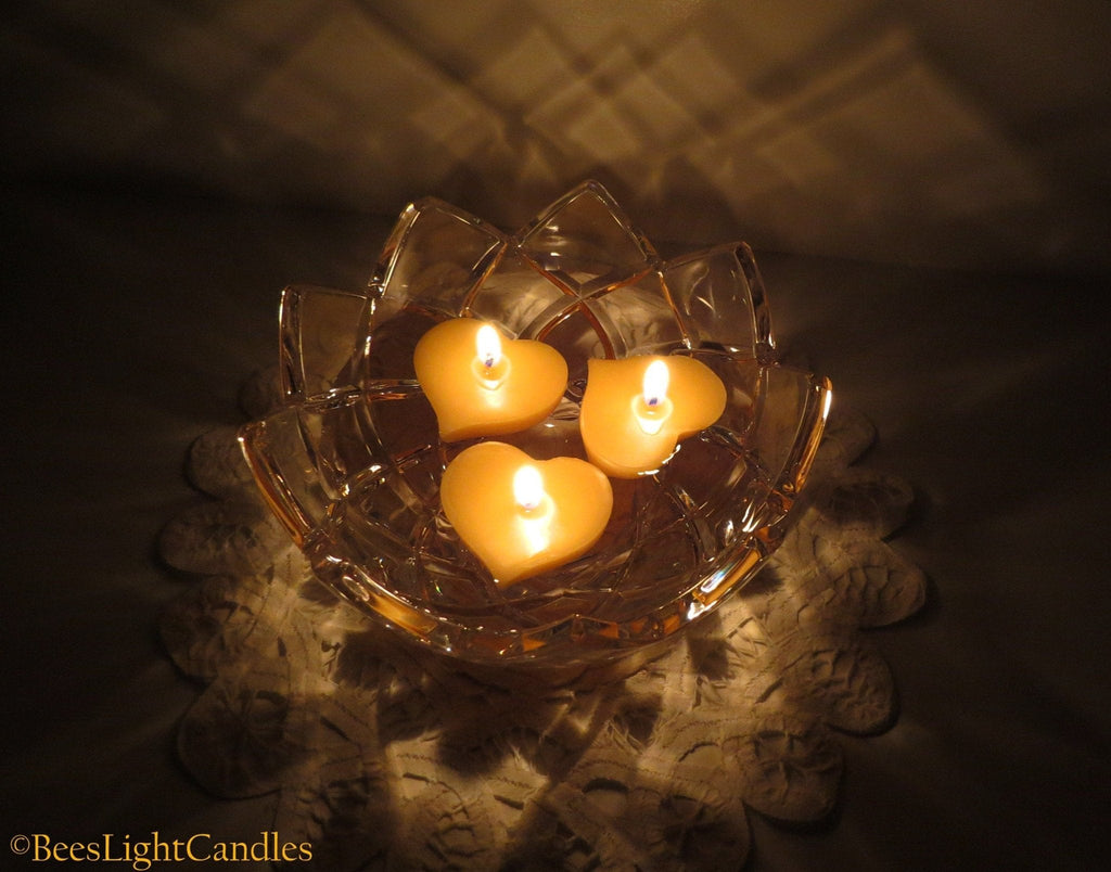 Floating heart-shaped candles in a clear glass bowl, four lit wicks visible