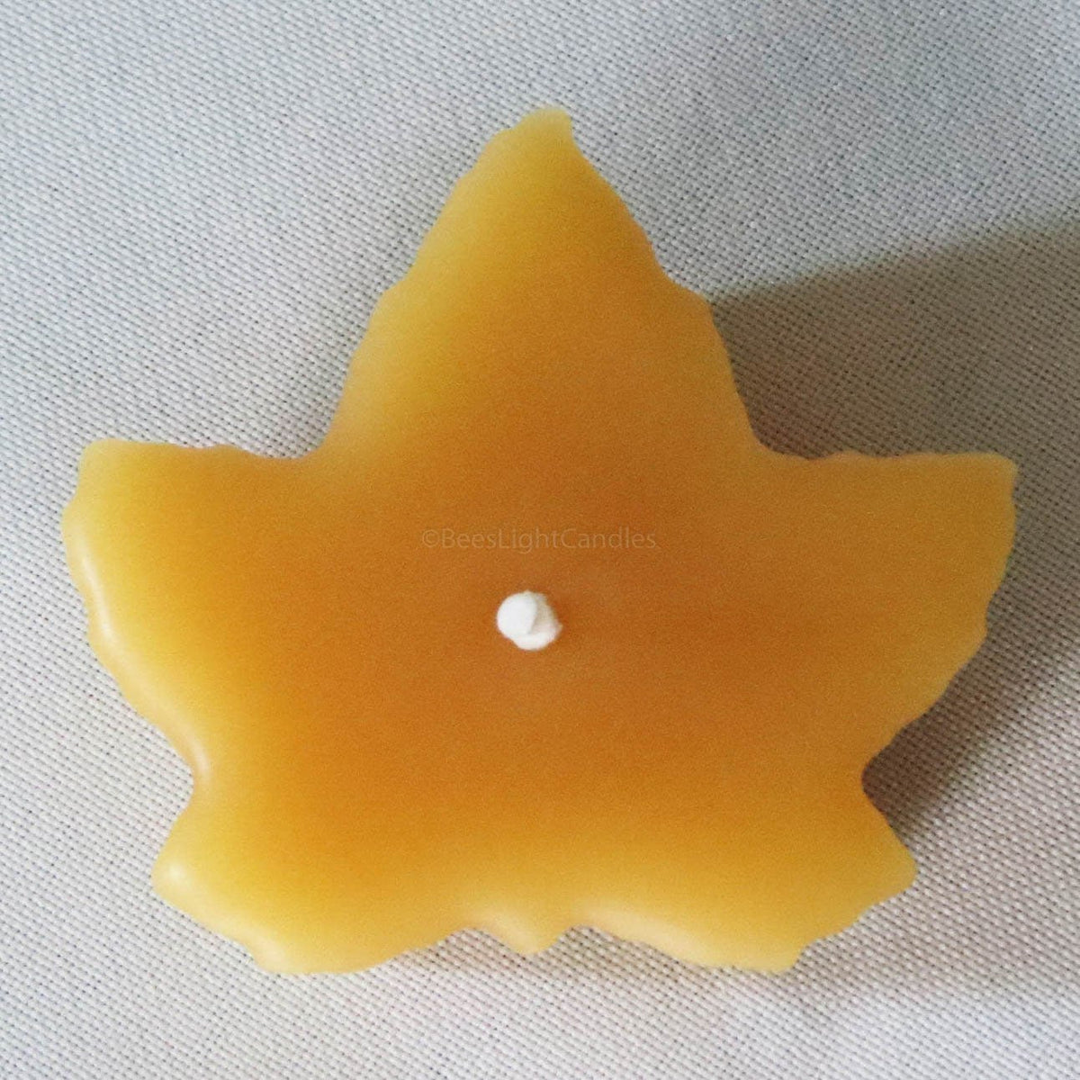 Yellow maple leaf beeswax candle with centered melt pool and unlit wick