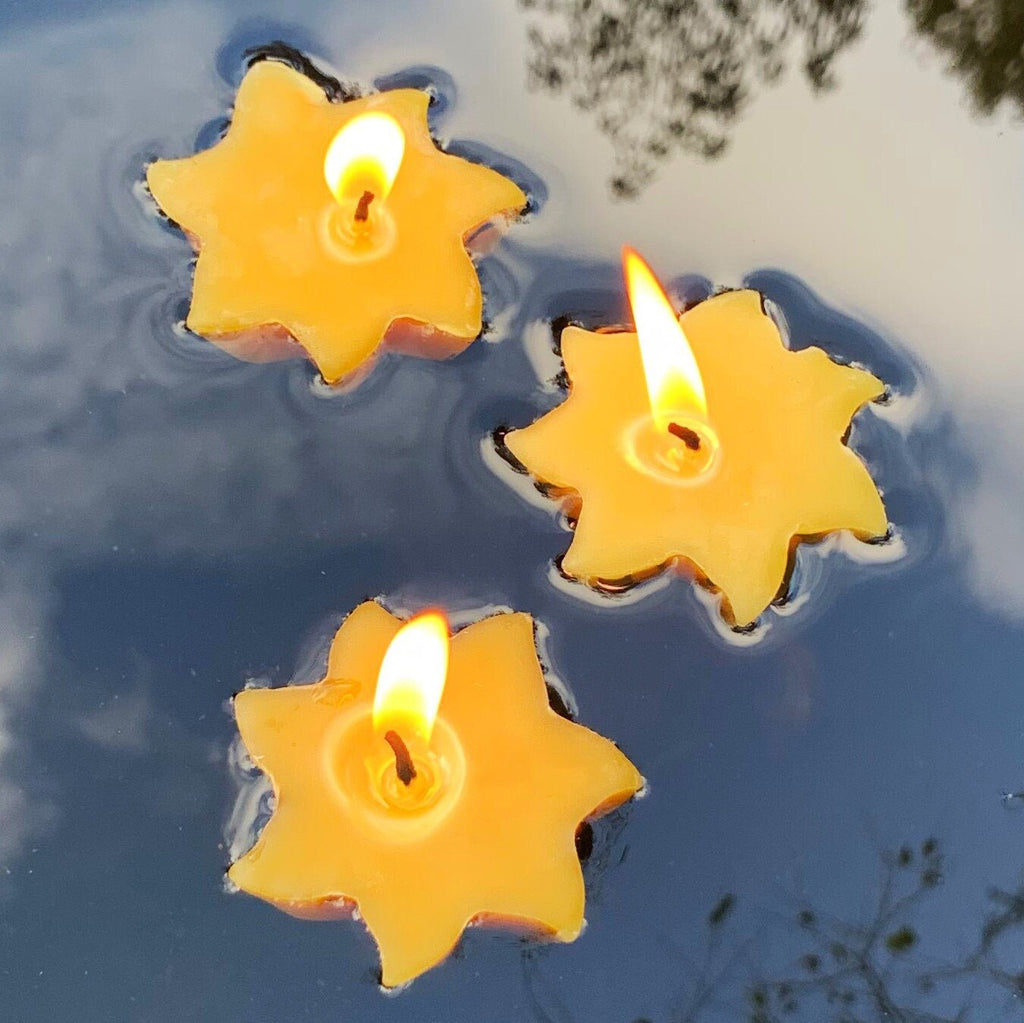 Three lit star-shaped yellow floating beeswax candles in water