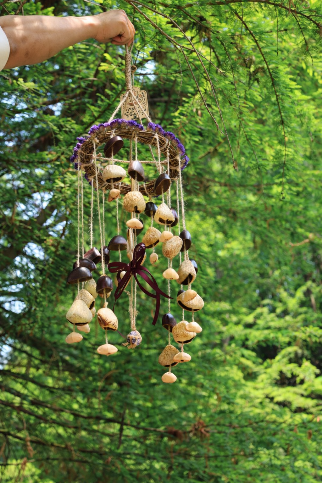 Vine wreath seed chime held in hand, with purple flowers, bells, and seed pods