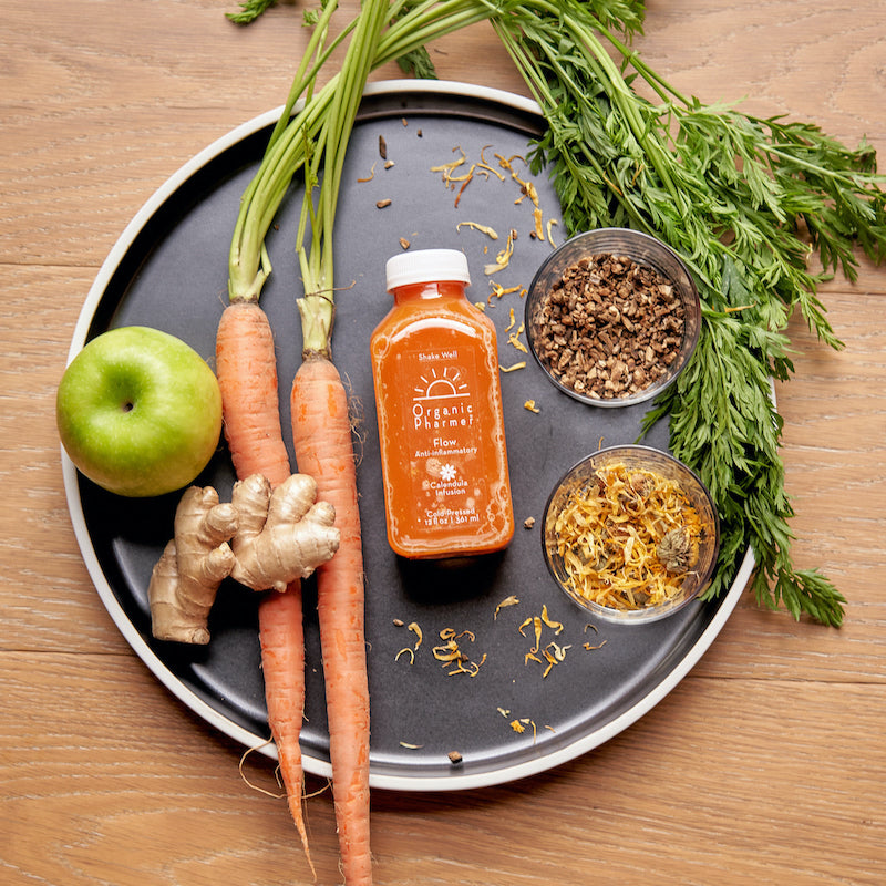 Organic botanical beverage bottle with carrots, ginger, apple, and dried herb bowls