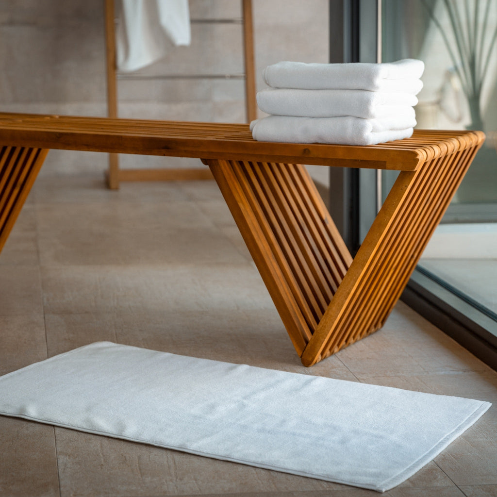 Light blue bath mat on tile floor near a wooden bench