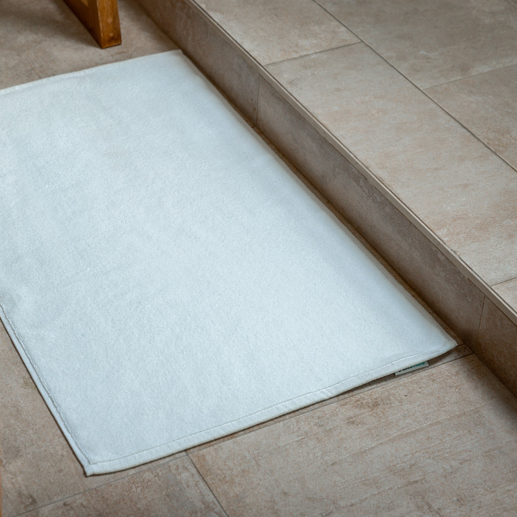 White bath mat on tile floor with stitched edge border