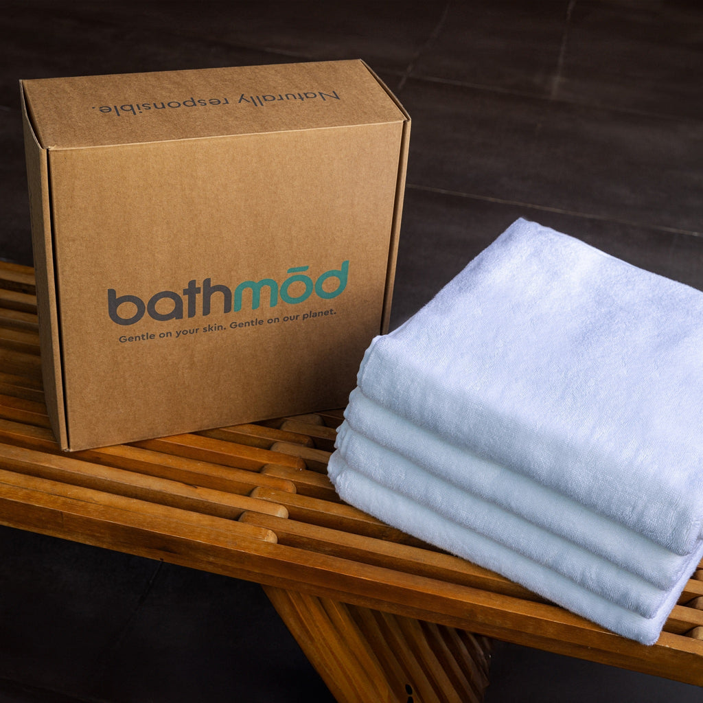 Four white organic bath towels folded beside a Bathmod box