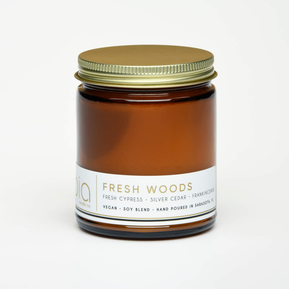 Amber candle jar with green metal lid and Fresh Woods label, unlit
