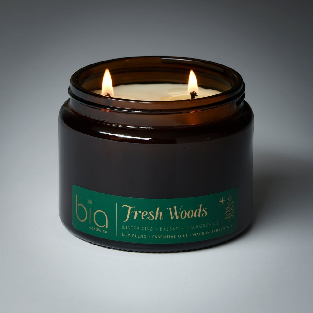 Dark glass Fresh Woods candle jar with two lit wicks