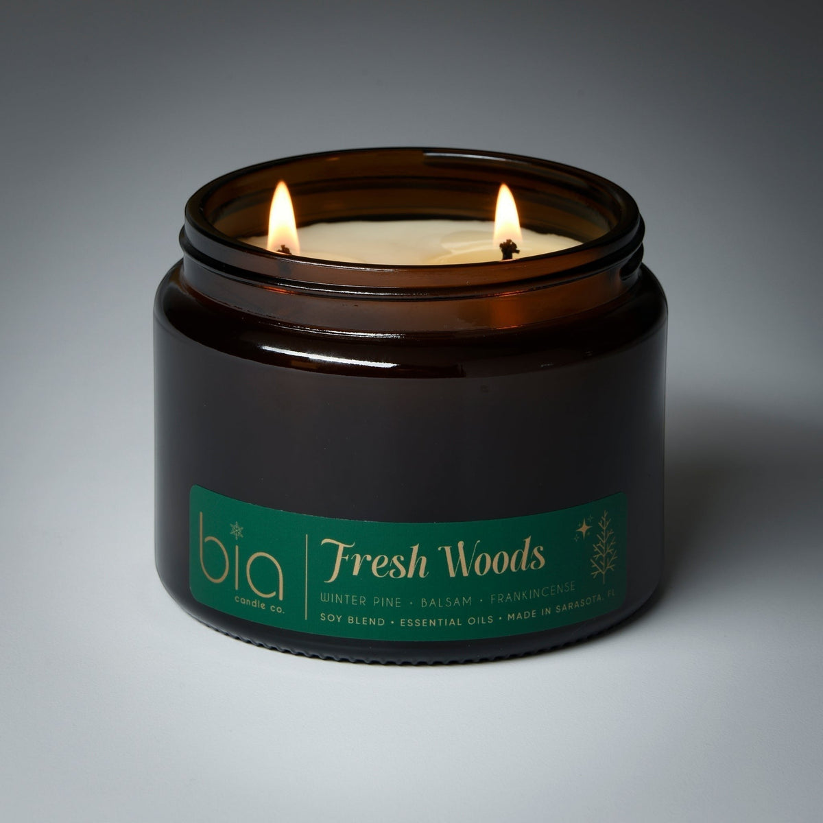Dark glass Fresh Woods candle jar with two lit wicks