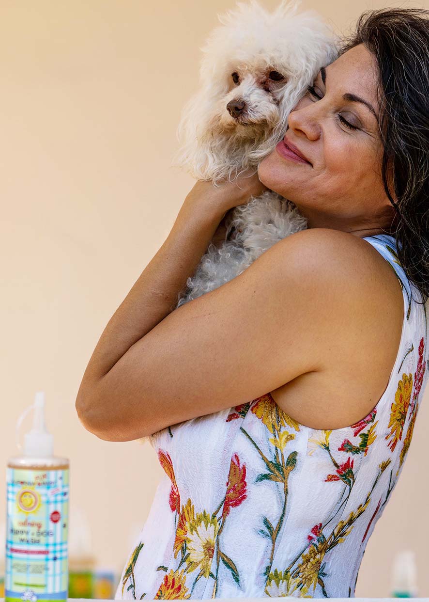 Small white dog in arms with puppy and dog wash bottle in foreground