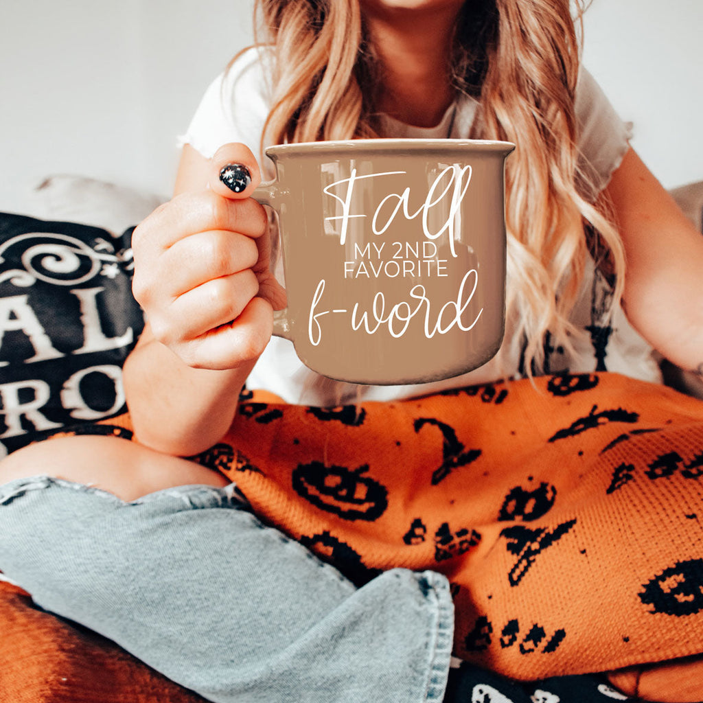 Brown ceramic coffee mug with white “fall” and “f-word” lettering held close-up