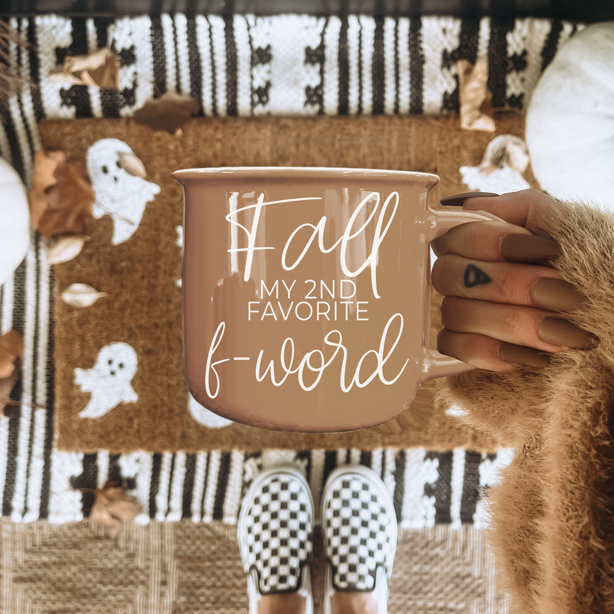Beige mug with white quote in hands, set on a cozy blanket with ornaments