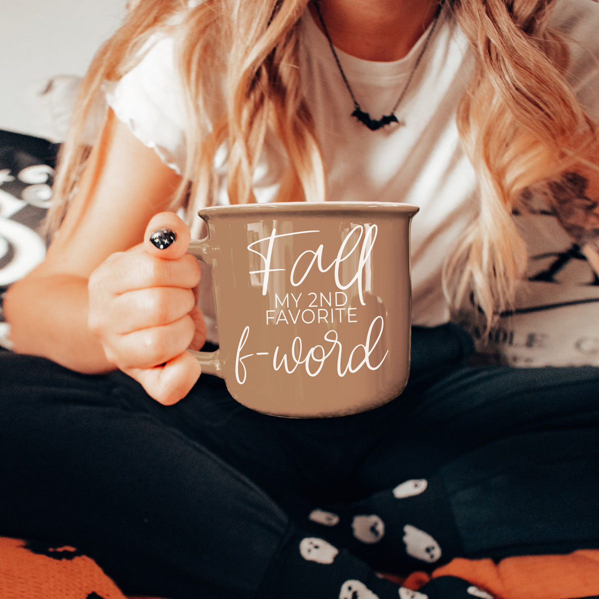 Brown ceramic coffee mug with white “fall” and “f-word” lettering held while seated