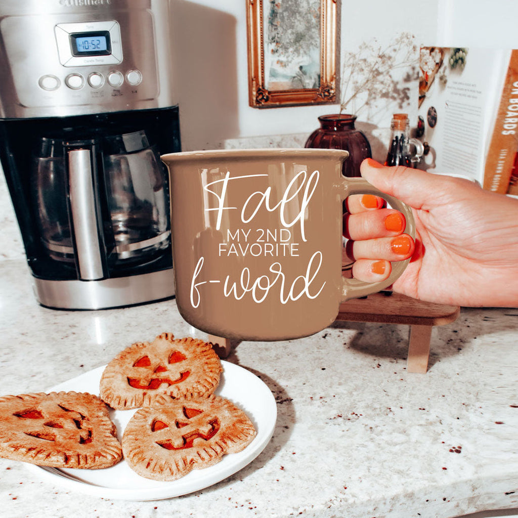 Brown ceramic coffee mug with white “fall” and “f-word” lettering in kitchen setting