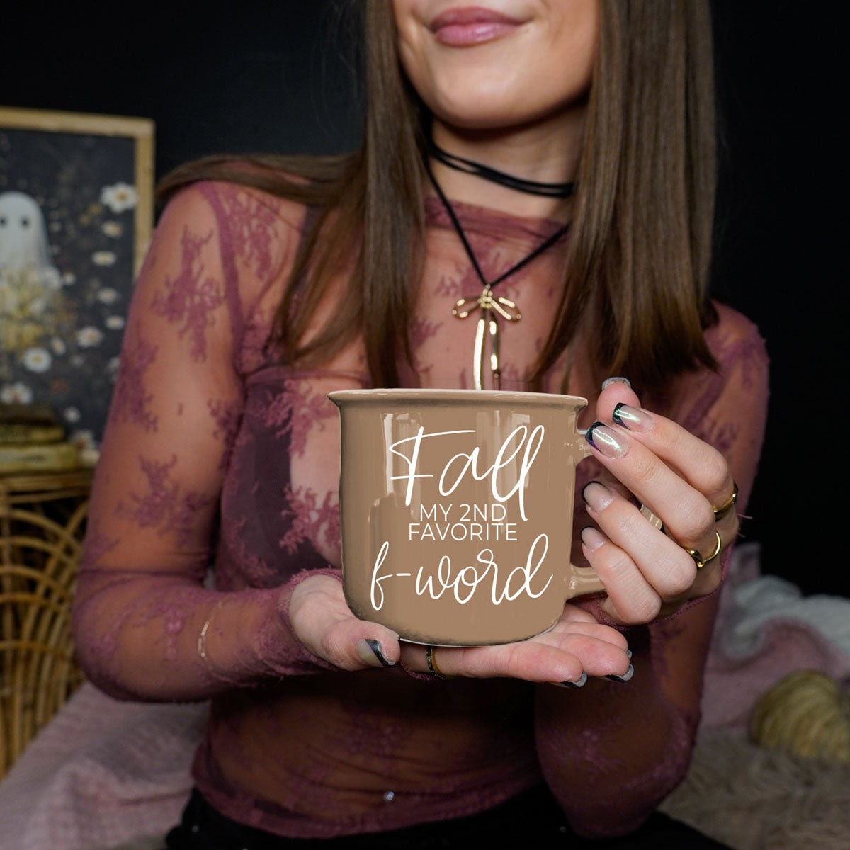 Brown ceramic coffee mug with white “fall” and “f-word” lettering held at chest level