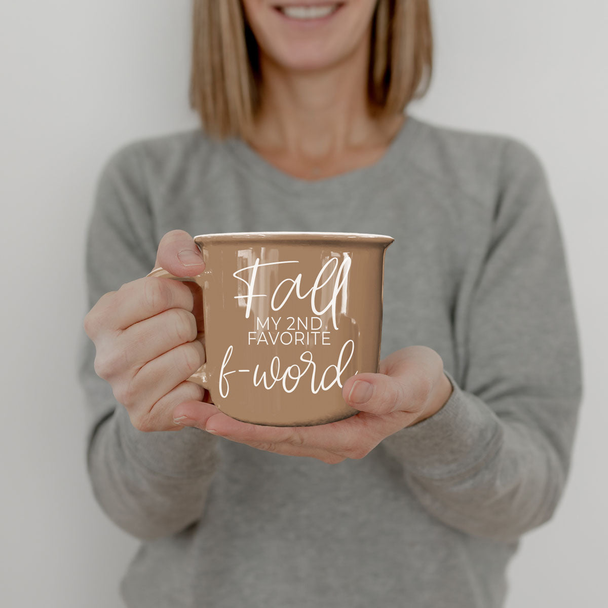 Brown ceramic mug with white “fall” and “f-word” text held with both hands