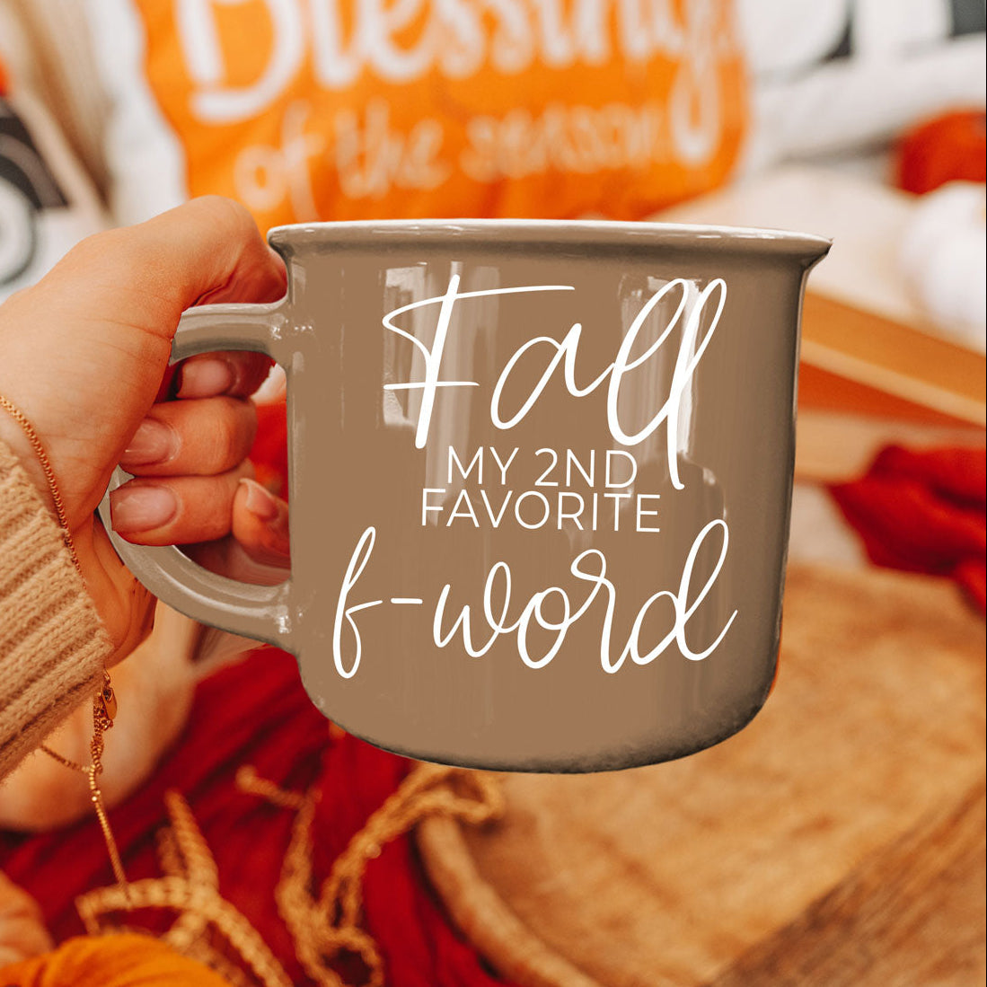 Close-up taupe ceramic mug with white 'Fall' quote, held by a hand
