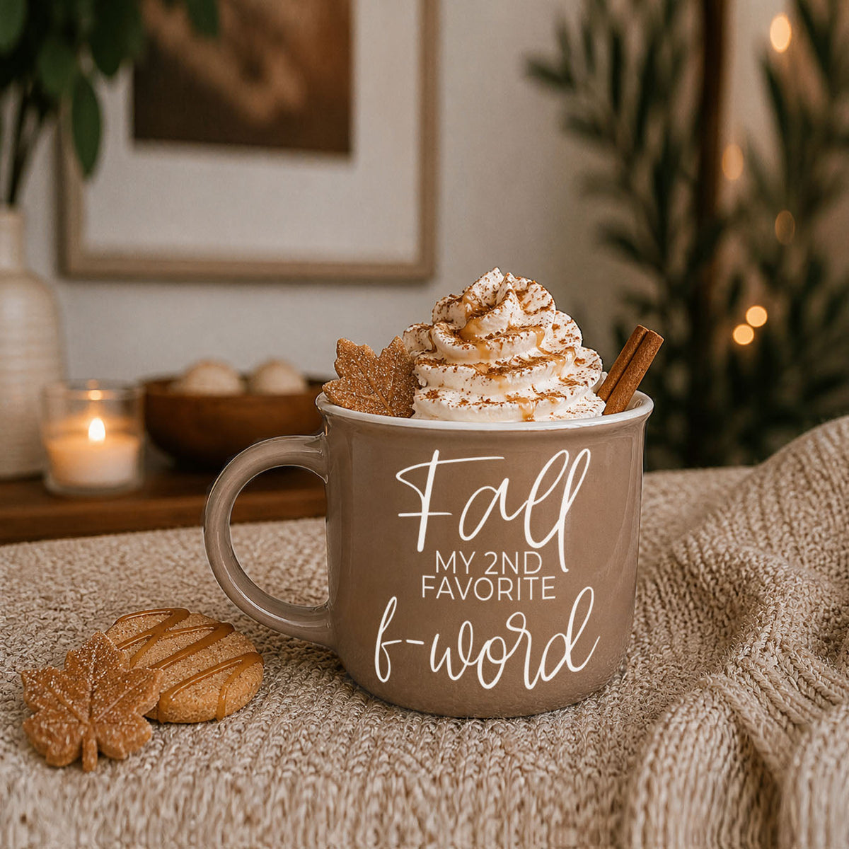 Beige ceramic mug with white lettering on a soft blanket, topped with whipped cream