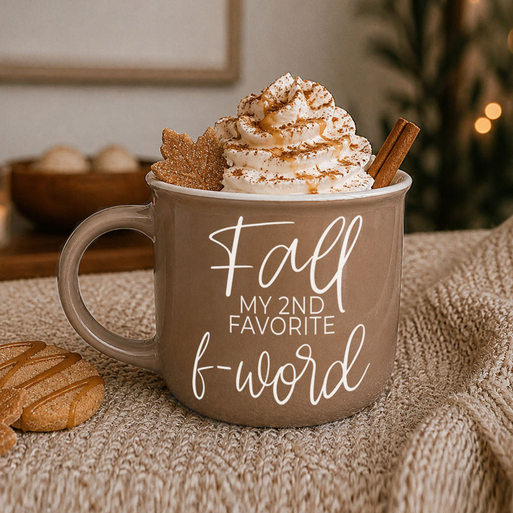 Taupe ceramic mug with white 'Fall' quote resting on a knit blanket