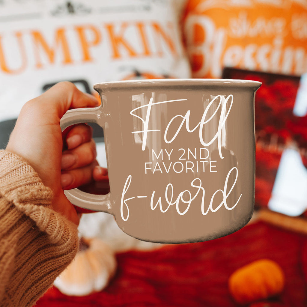 Taupe ceramic mug with white 'Fall' quote and side handle, held in a hand