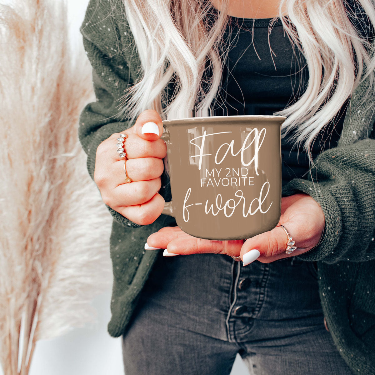Taupe mug held in front of the body with white 'Fall' quote, dark sweater sleeves