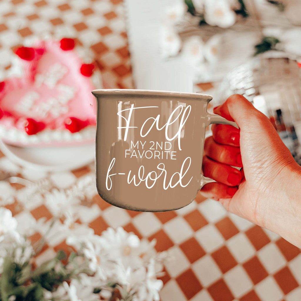 Taupe ceramic mug with white 'Fall' quote held close in a hand