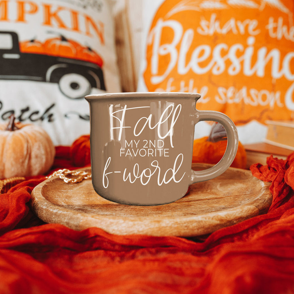 Taupe ceramic mug with white 'Fall' quote centered on a round wooden surface