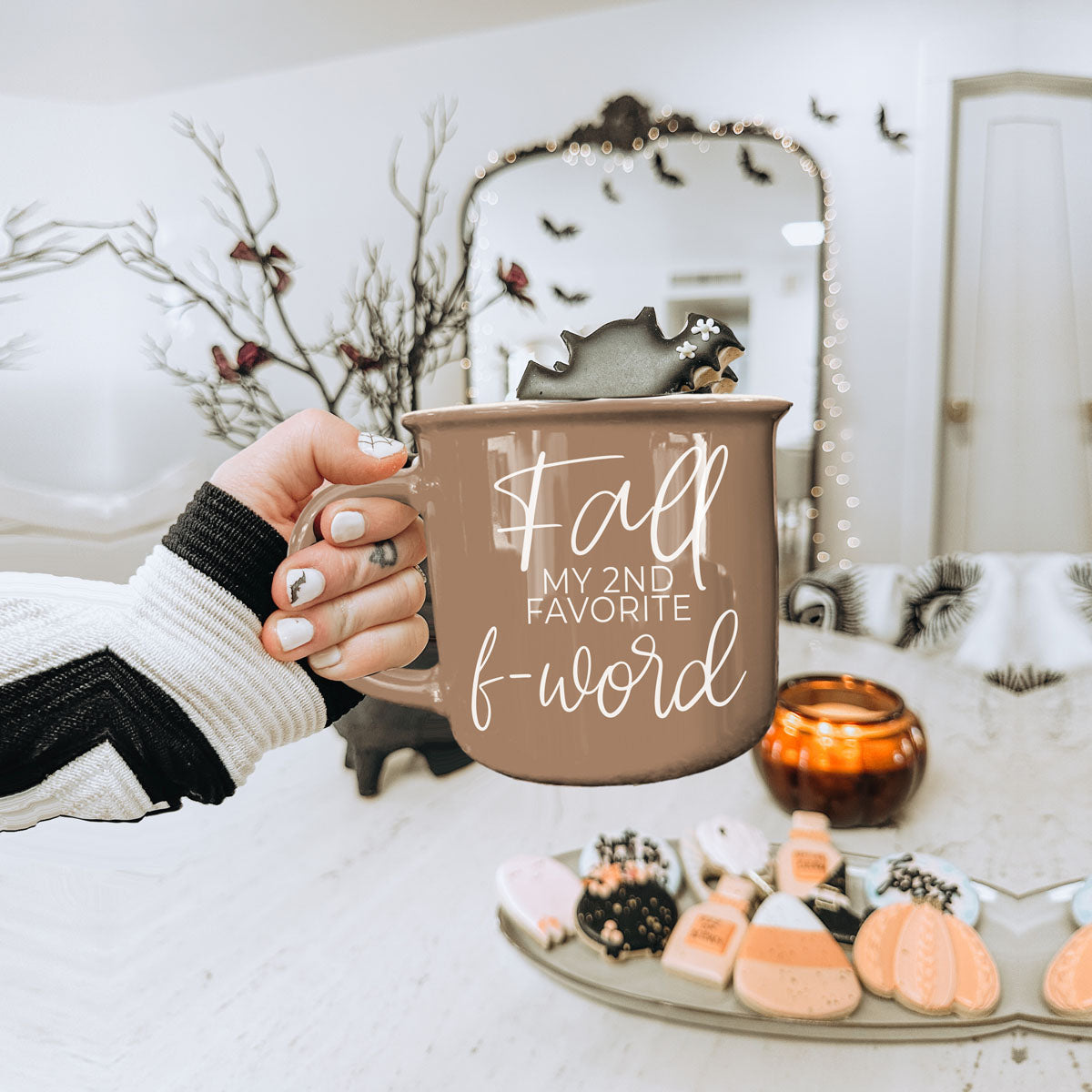 Beige mug with white script quote held in a hand near seasonal lights and decor