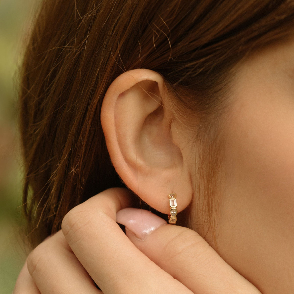 Gold hoop earring with rectangular gemstones held near ear