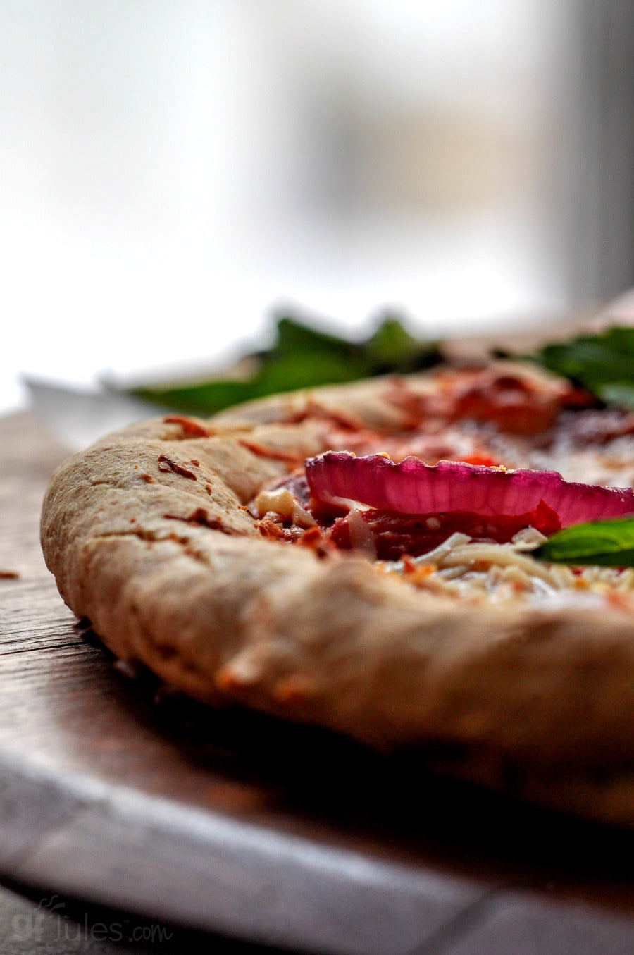 Close-up of gluten-free pizza crust with tomato topping, onions, and basil