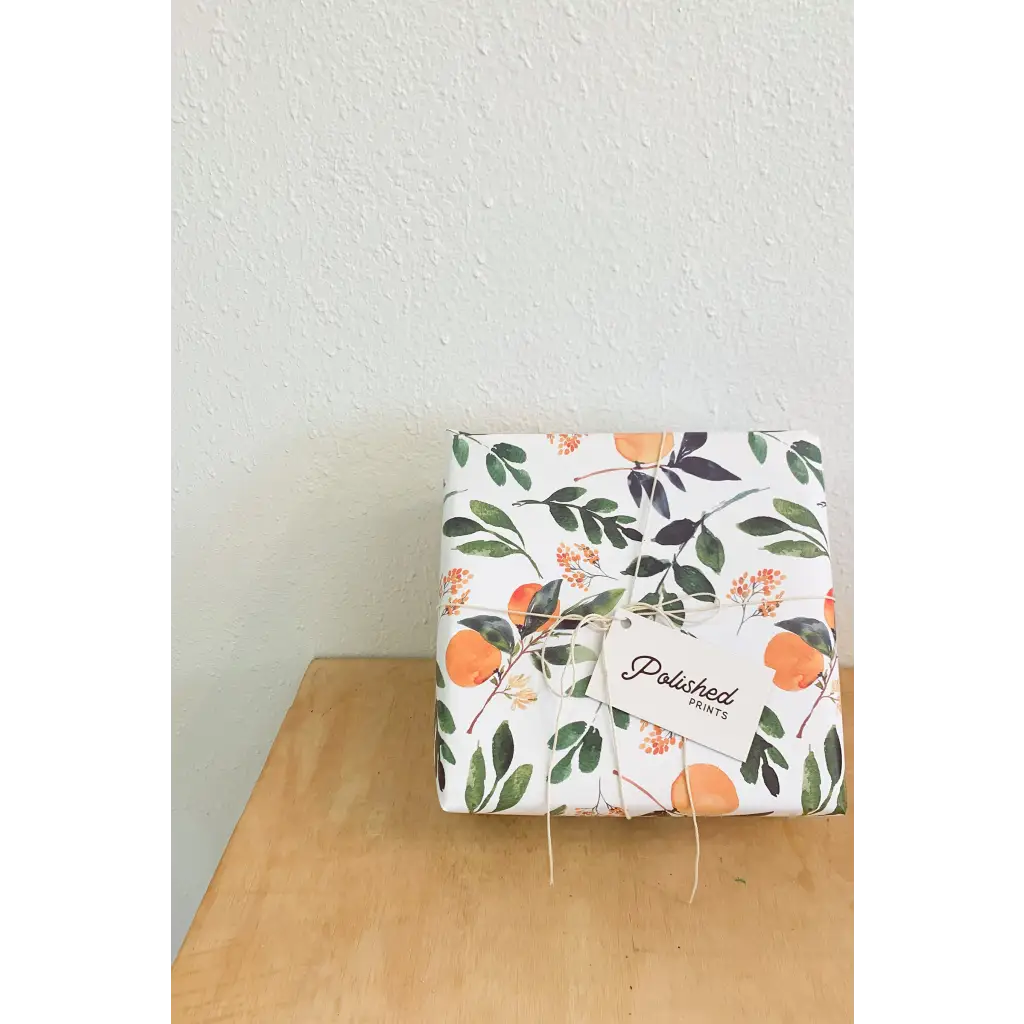 Floral gift wrapping paper with orange fruit and green leaves, tied with string, tag.
