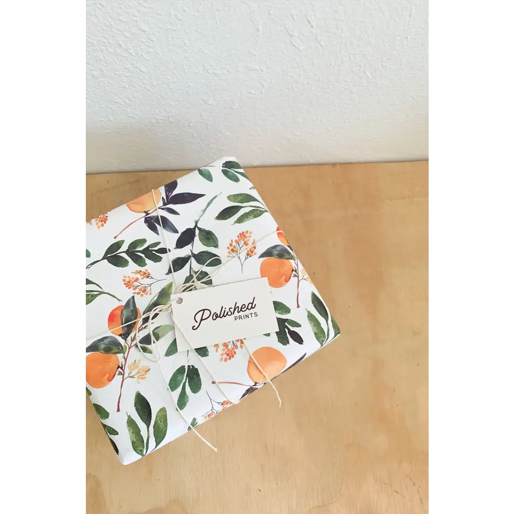 Floral wrapped gift box with orange fruit and green leaves, string tie, Polished Prints tag.
