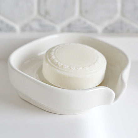 White glossy porcelain soap dish with raised rim and centered soap bar