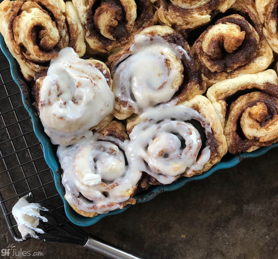 Gluten-free flour cinnamon rolls with white icing on a blue tray.